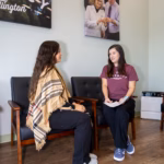 Women seated under pharmacy wall art.
