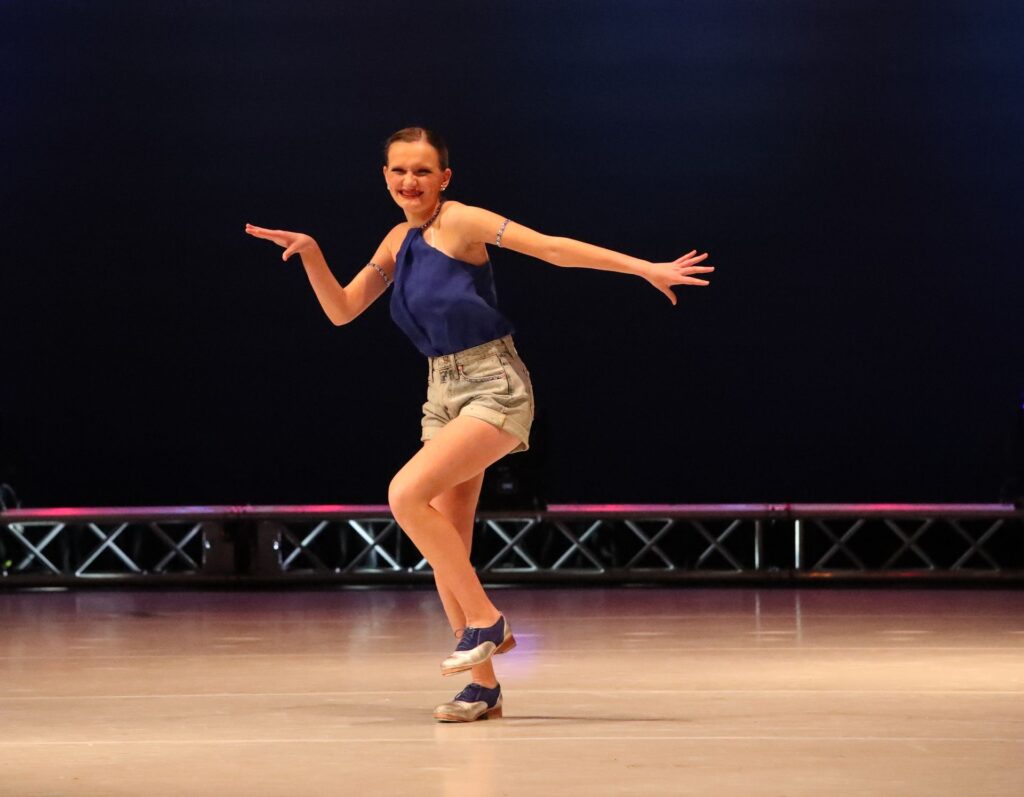Tap dancer performing on stage in blue top.
