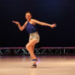 Tap dancer performing on stage in blue top.
