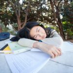Student napping on study materials outside